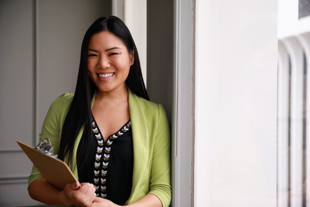 A woman with long black hair is smiling while holding a clipboard